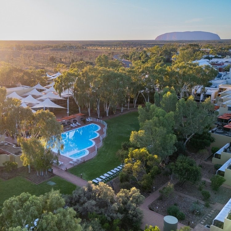 Ayers Rock Resort pool surrounded by greenery with Uluru in the distance